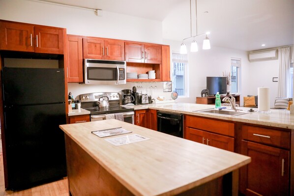 A modern kitchen with wooden cabinets, a black refrigerator, a microwave, a stove, and a sink.