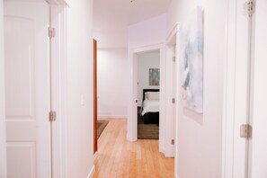 A hallway with wooden flooring, white walls, and a bed in the background.