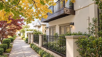 A residential street with a sidewalk, a black metal fence, and houses with balconies.