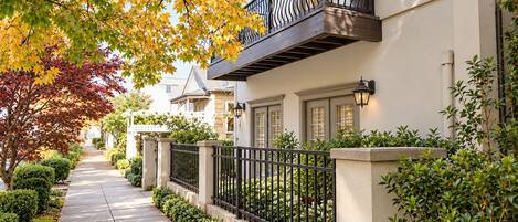 A residential street with a sidewalk, a black metal fence, and houses with balconies.