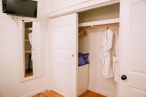 A white closet with a television mounted above it, a mirror on the left, and several white robes hanging on a rack.