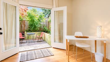A room with a sliding glass door leading to an outdoor patio with a table and chairs, a white desk with a tray, and a white bucket.