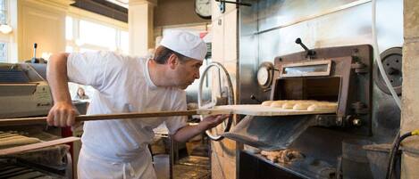 Eine Person in weißer Uniform bedient einen großen Industrieofen, vermutlich zum Backen oder Kochen, in einer gewerblichen Küche.