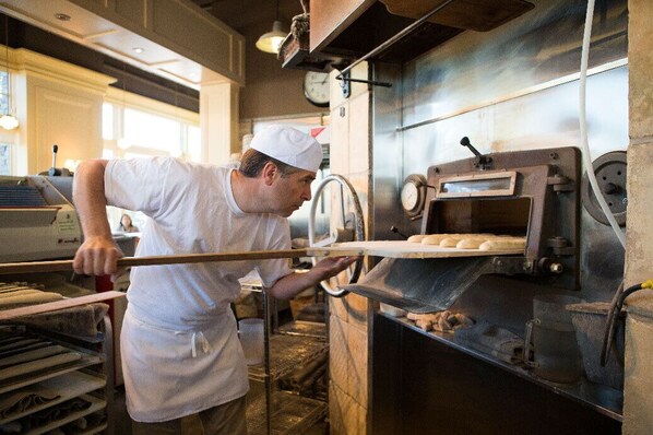 A person in a white uniform operating a large industrial oven, likely for baking or cooking, in a commercial kitchen setting.