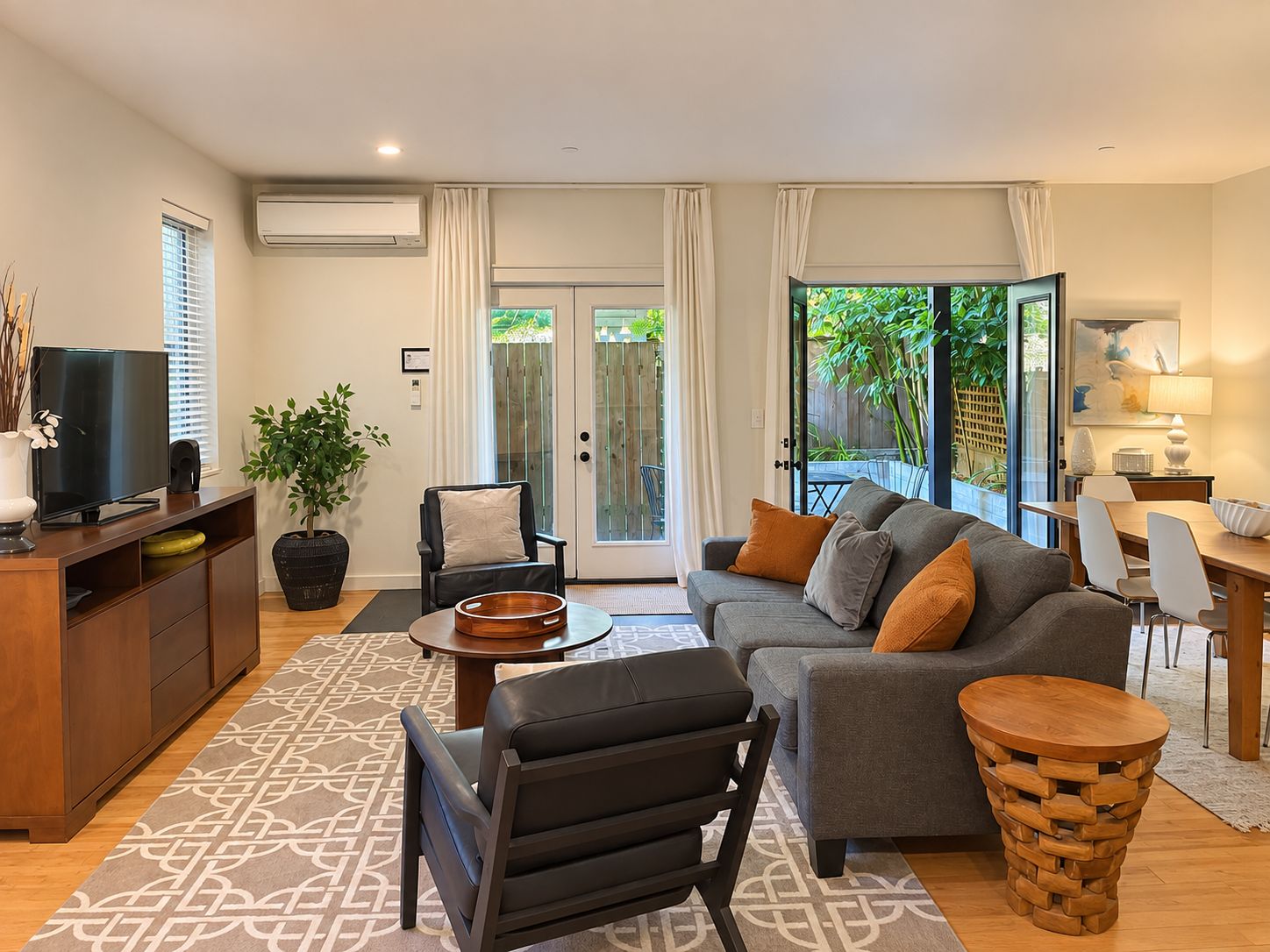 A modern living room with a sofa, a TV, a dining table, and a large window.