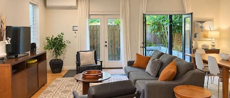 A modern living room with a sofa, a TV, a dining table, and a large window.