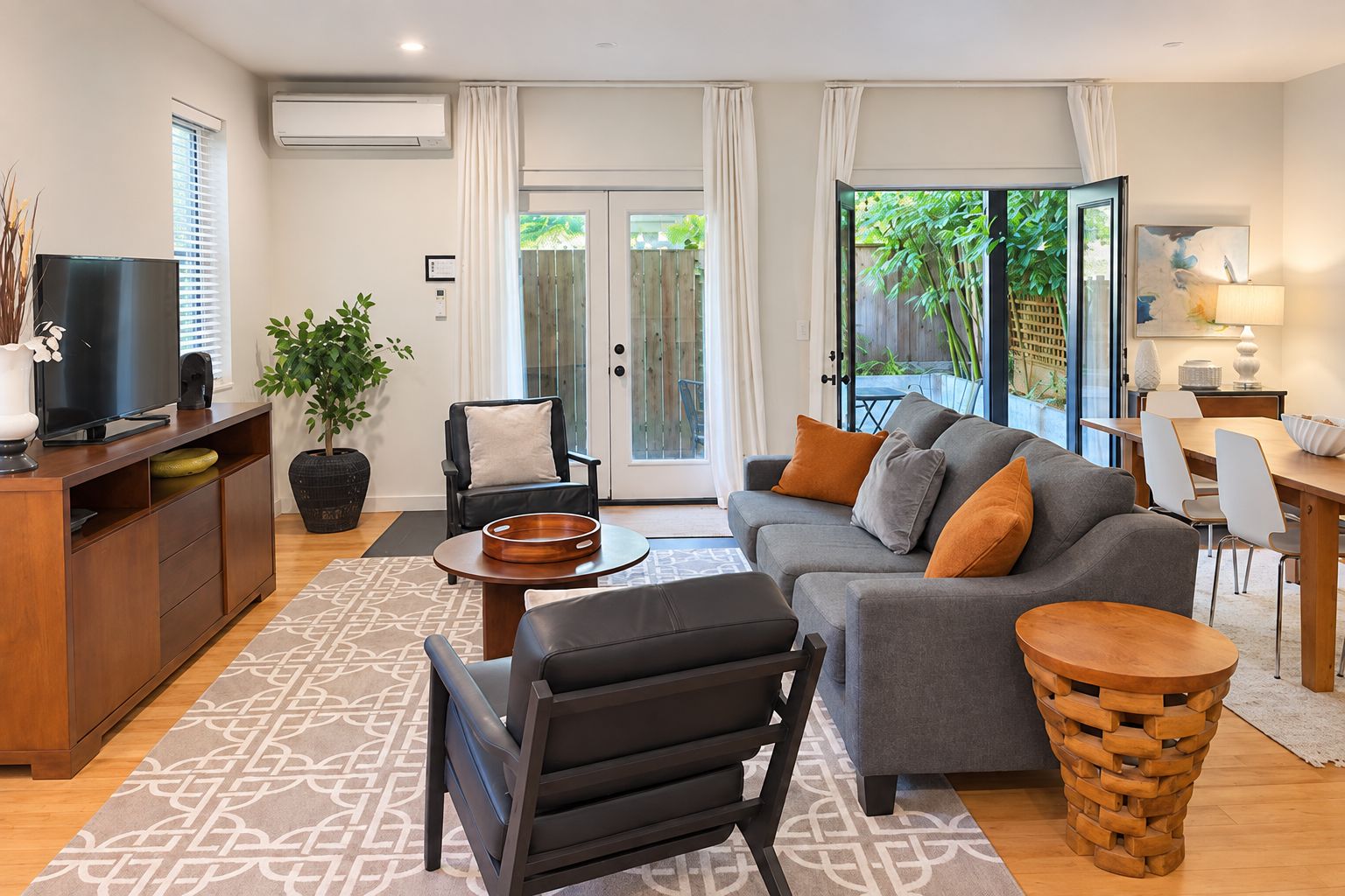A modern living room with a sofa, armchairs, a coffee table, and a TV. There is a dining area with a table and chairs.