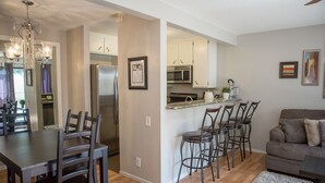 Una cocina moderna con electrodomésticos de acero inoxidable, una zona de comedor con mesa y sillas de madera, y una sala de estar con sofá y una mesita de centro.