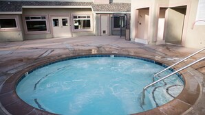 Una piscina con borde de azulejos, una escalera metálica y un edificio con fachada color beige y ventanas al fondo.