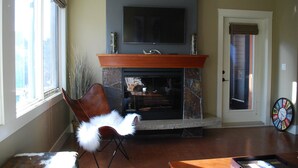 Una sala de estar con chimenea, un televisor montado encima y una puerta con ventana, además de un reloj en la pared.