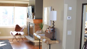 Una sala de estar con chimenea, una silla, una mesa y una lámpara.