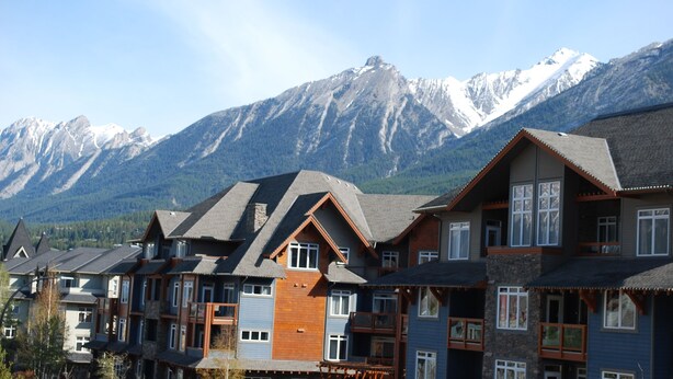 Una hilera de casas de madera con varios pisos y grandes ventanales, con montañas nevadas al fondo.