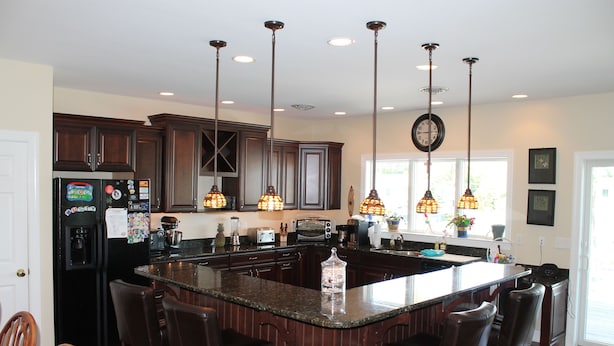 A modern kitchen with a central island, dark wooden cabinets, and pendant lighting.
