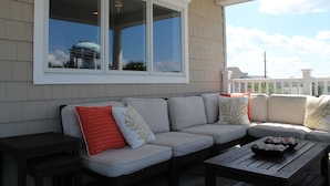 A covered outdoor seating area with a sofa and a table, large windows, and a view of a water tower.