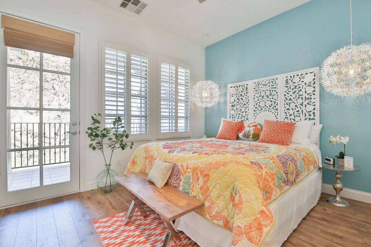Une chambre à coucher avec un grand lit, un banc, une petite table sur laquelle est posé un vase, et un panneau décoratif au mur.