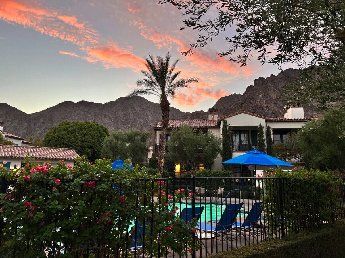 A pool area with lounge chairs and umbrellas, surrounded by greenery and a mountain backdrop.