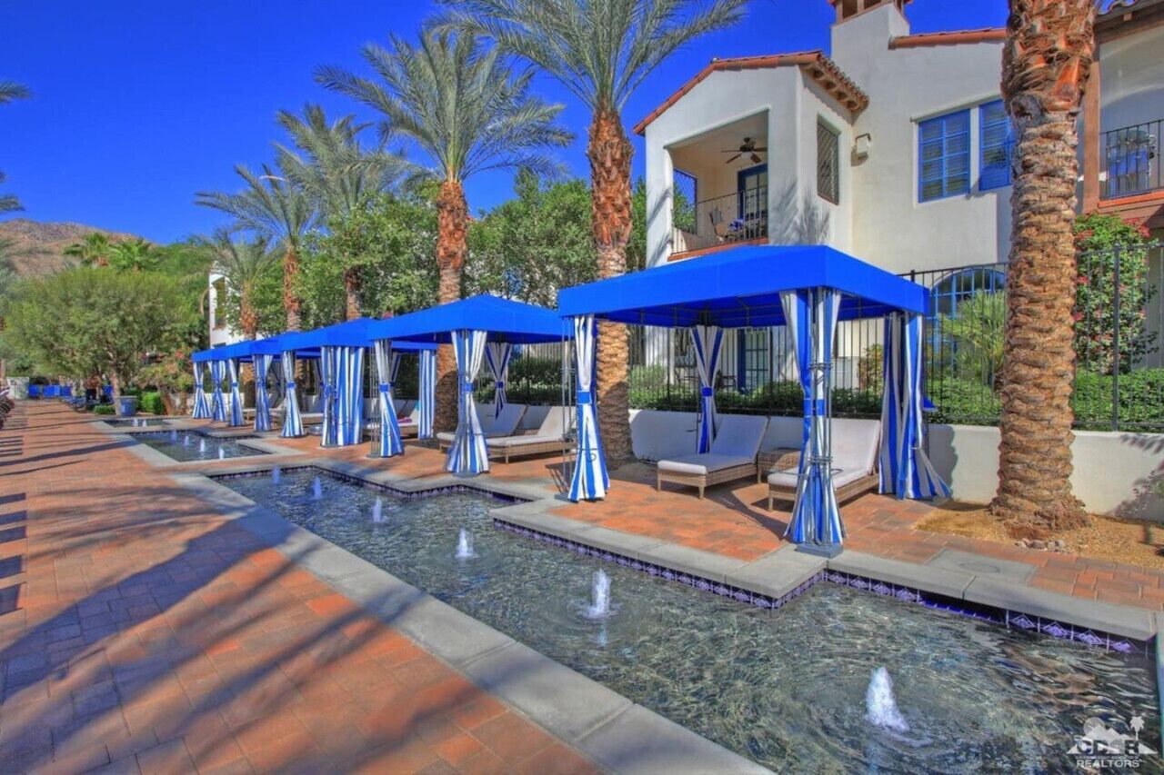 Un espace piscine agrémenté de parasols bleus, de chaises longues et de palmiers.