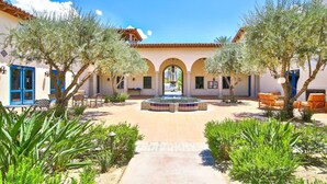 A courtyard with a fountain, outdoor seating, and a building with arches and a tiled roof. - La Villa #1 * Townhouse * 12 Pools *WoW Views (La Quinta)