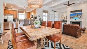 A spacious living area with a wooden dining table, leather chairs, a brown leather sofa, a fireplace, and a television mounted on the wall. - La Villa #1 * Townhouse * 12 Pools *WoW Views (La Quinta)