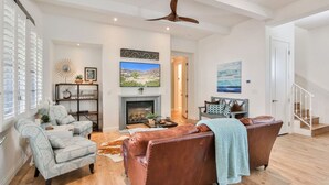A spacious living room with a fireplace, a ceiling fan, and a staircase leading to another level. - La Villa #1 * Townhouse * 12 Pools *WoW Views (La Quinta)