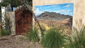 Edifici rústic amb una porta marró desgastada, envoltat de gespa seca i arbustos.