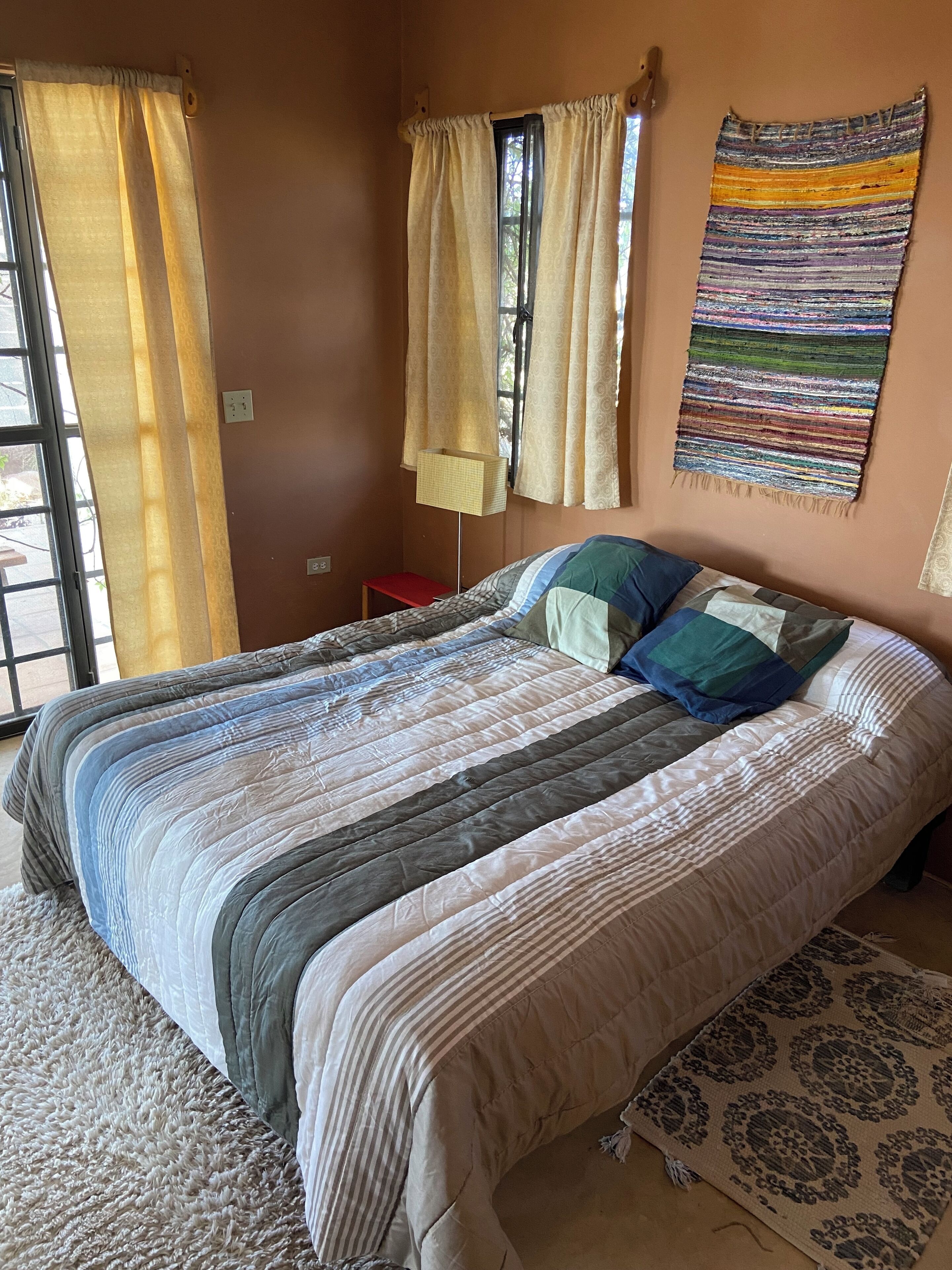 A bed with a striped bedspread, a red nightstand, and a patterned rug.