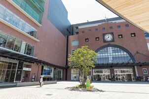 Un edificio moderno con un gran reloj, un árbol en el centro y un letrero con texto en idioma extranjero.