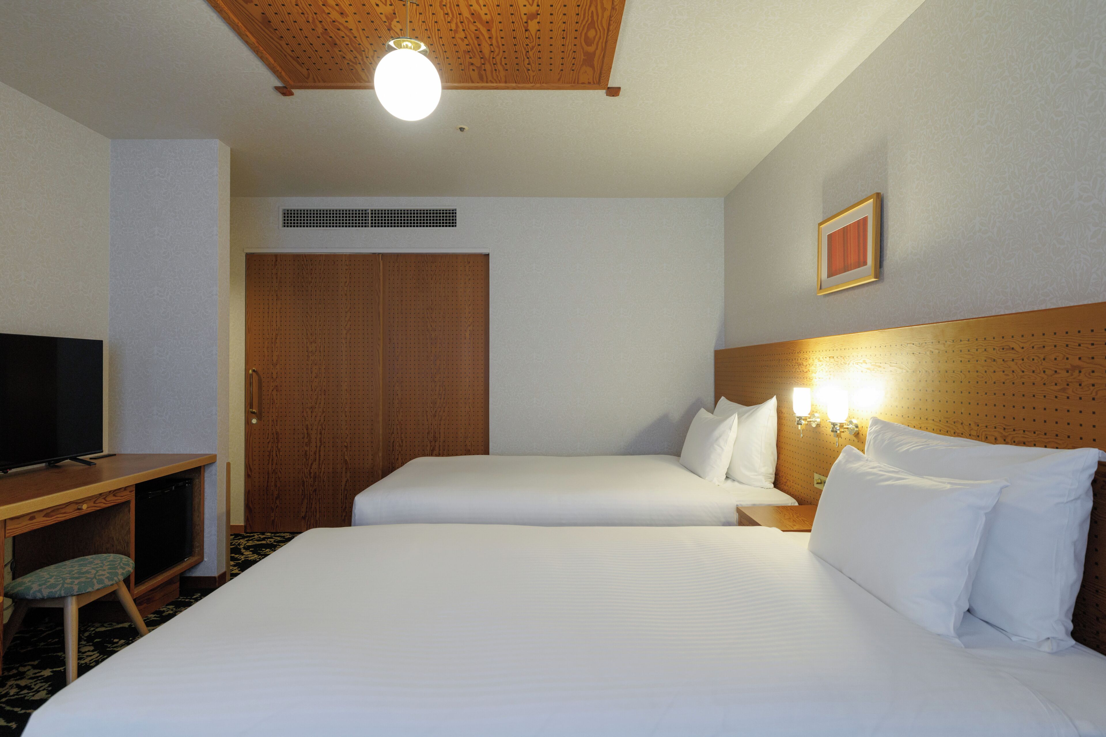 A hotel room with two beds, a desk with a television, and a wooden ceiling.