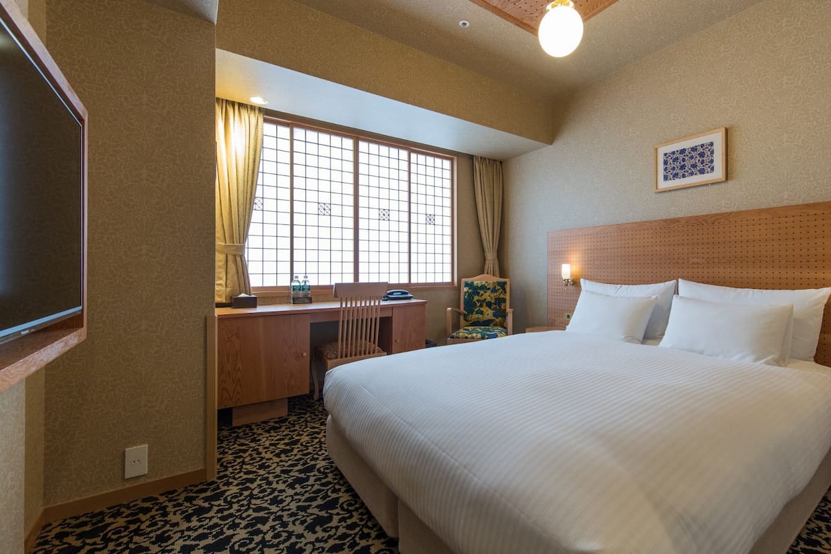 A hotel room with a bed, desk, chair, and a television.