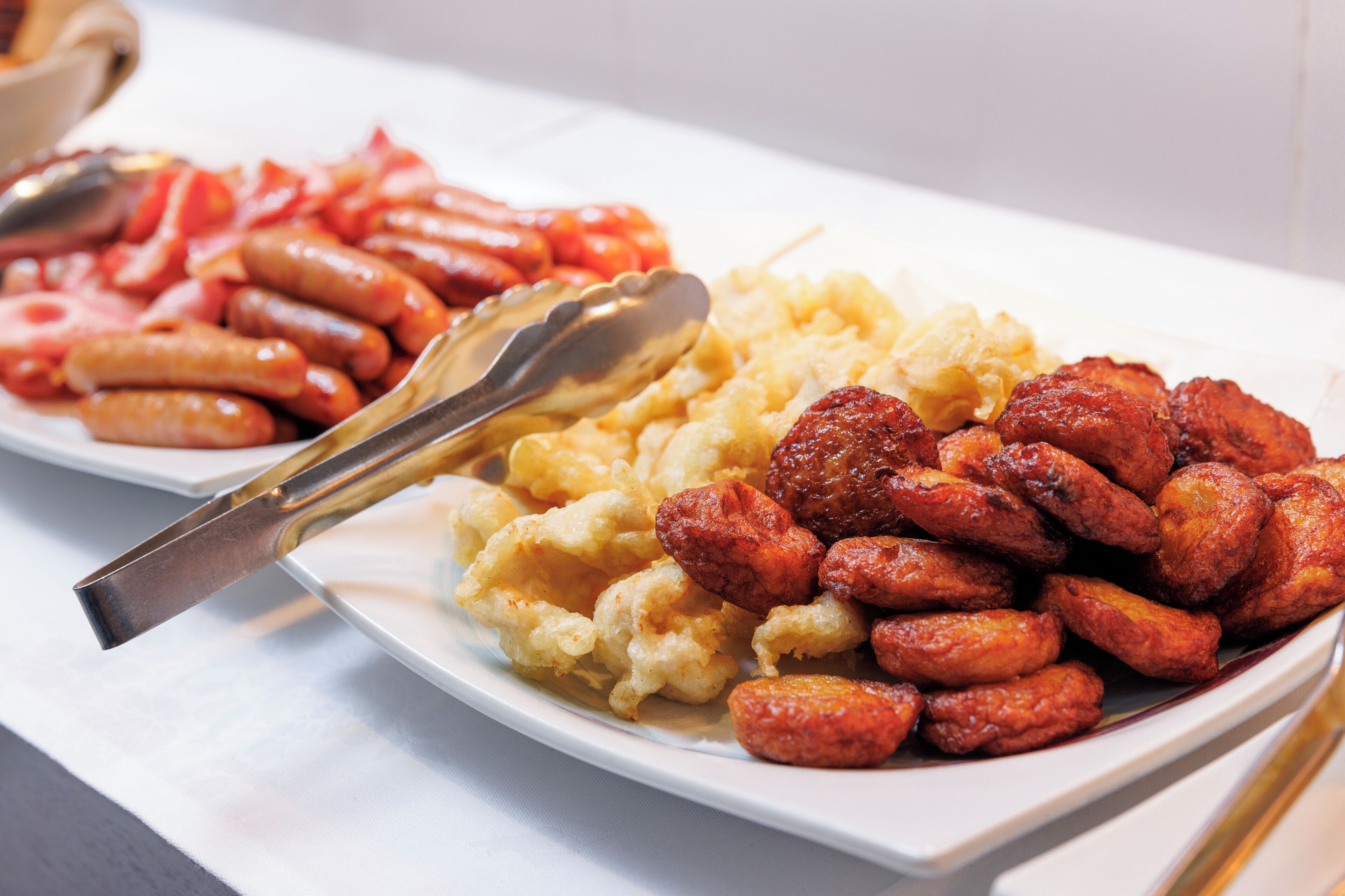 A plate of food including sausages, fried potatoes, and a spoon.