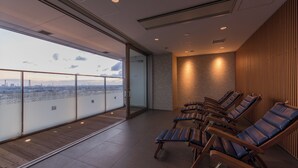 Un balcón interior moderno con vistas a la ciudad, sillones de madera y una pared de vidrio.
