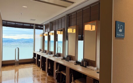 A row of sinks with mirrors, a sign for the powder room, and a view of the city and mountains through large windows.