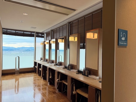 A row of sinks with mirrors, a sign for the powder room, and a view of the city and mountains through large windows.