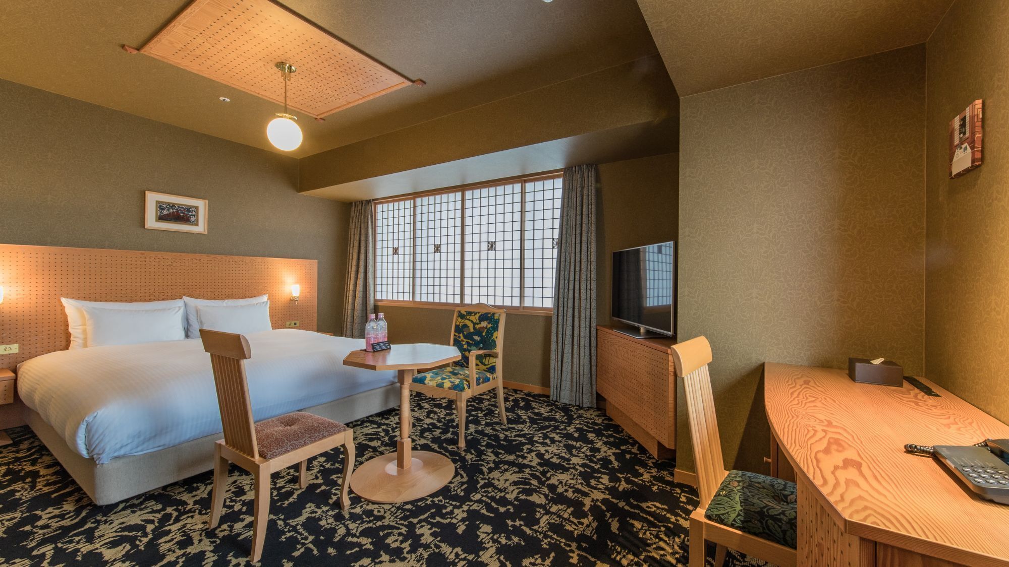 Une chambre d’hôtel avec un lit, un bureau, une chaise, une télévision et une fenêtre avec des rideaux.