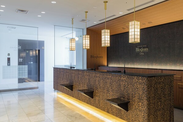 A reception desk with a patterned wall and three hanging pendant lights. - JR KYUSHU HOTEL Blossom Oita (Oita)