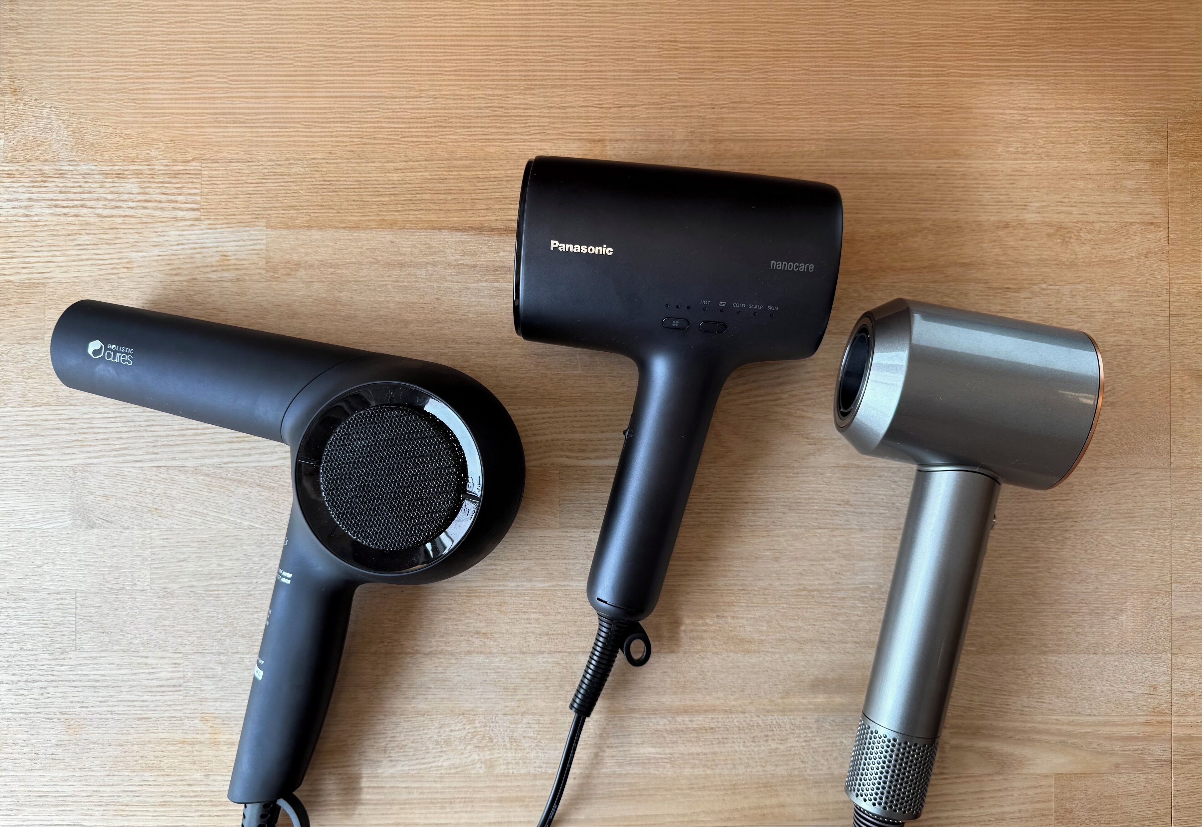 Three hair dryers on a wooden surface.