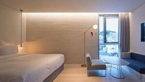 A modern hotel room with a large bed, a desk, and a view of the city through the window.