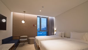 A modern hotel room with a large bed, a seating area with a table, and a view of the city through a window.
