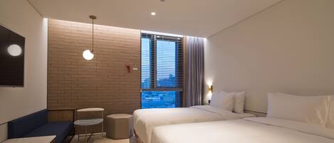 A modern hotel room with a large bed, a seating area with a table, and a view of the city through a window.