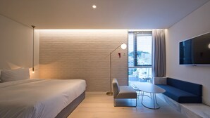 A modern hotel room with a bed, a desk, a chair, a TV, and a window with blinds.