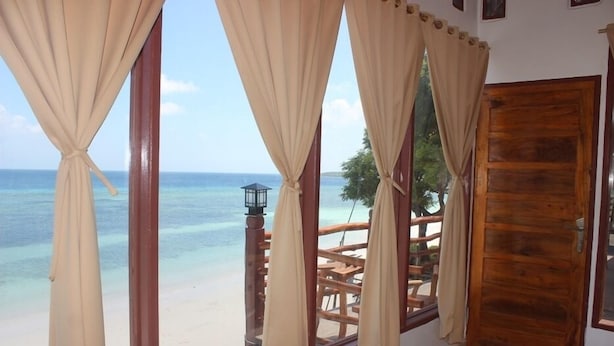 Una habitación con un gran ventanal con vista a una playa, una puerta de madera y vistas al océano.
