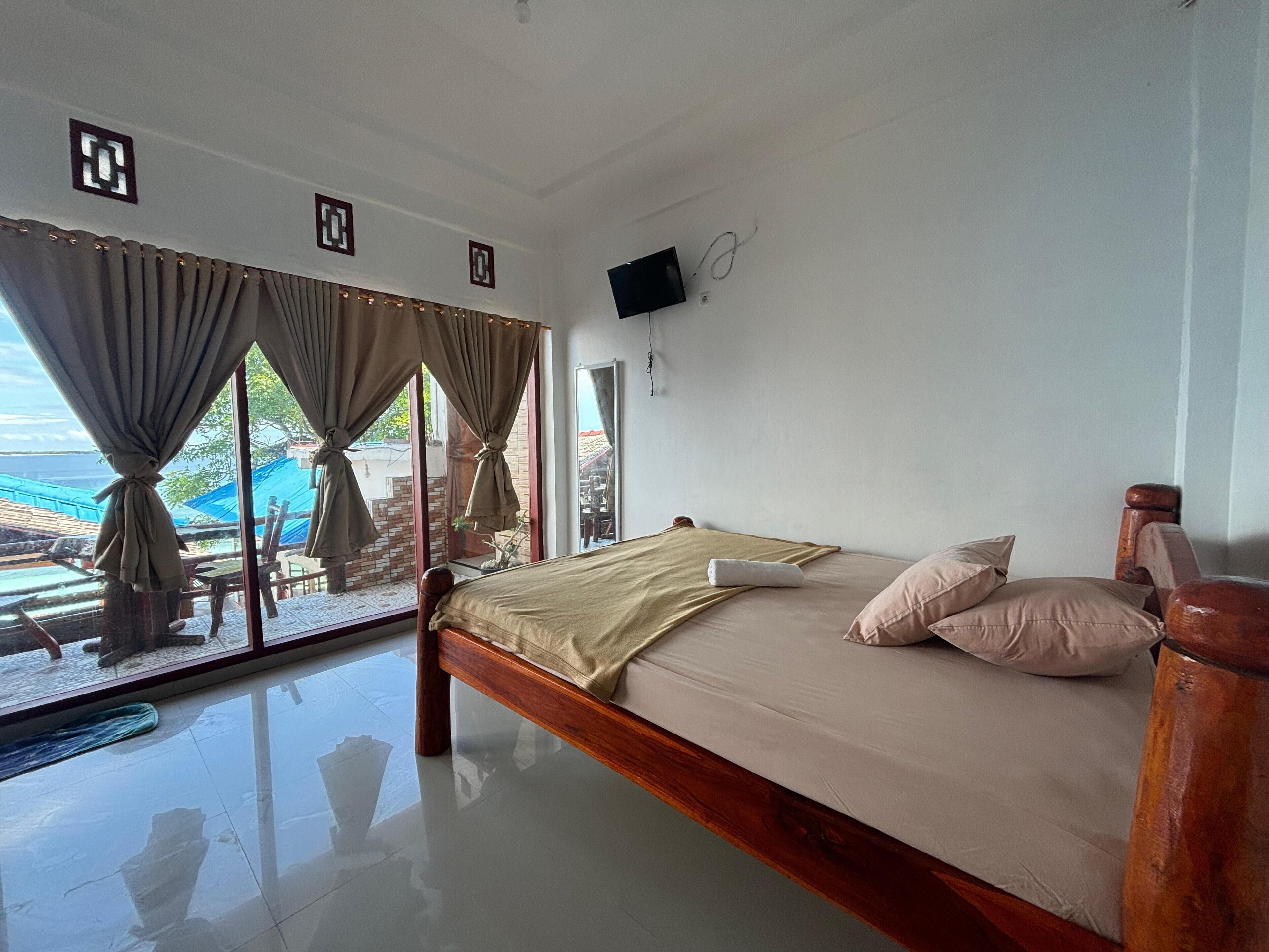 Un dormitorio con cama, cortinas, televisor y vista al exterior.