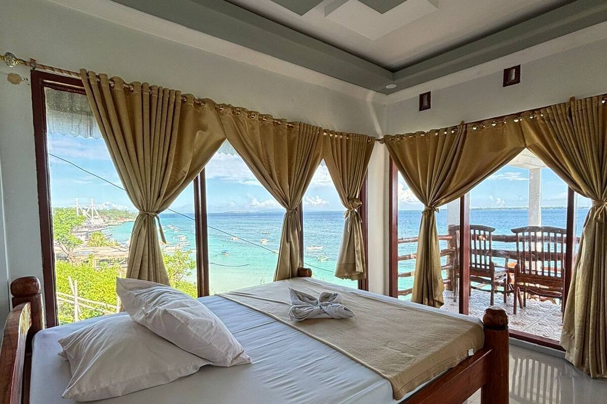 Una habitación con una cama grande, vista al mar y un balcón con baranda de madera.