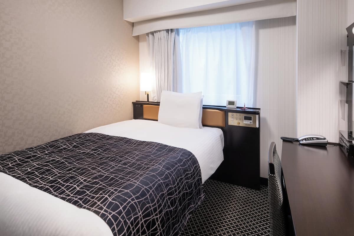 Une chambre d’hôtel avec un lit, une table de chevet avec une lampe, un téléphone et une fenêtre avec des rideaux.