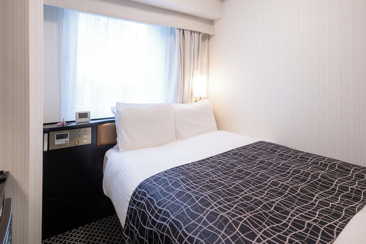 Une chambre d’hôtel avec un lit, un bureau équipé d’un ordinateur et une fenêtre avec des rideaux.