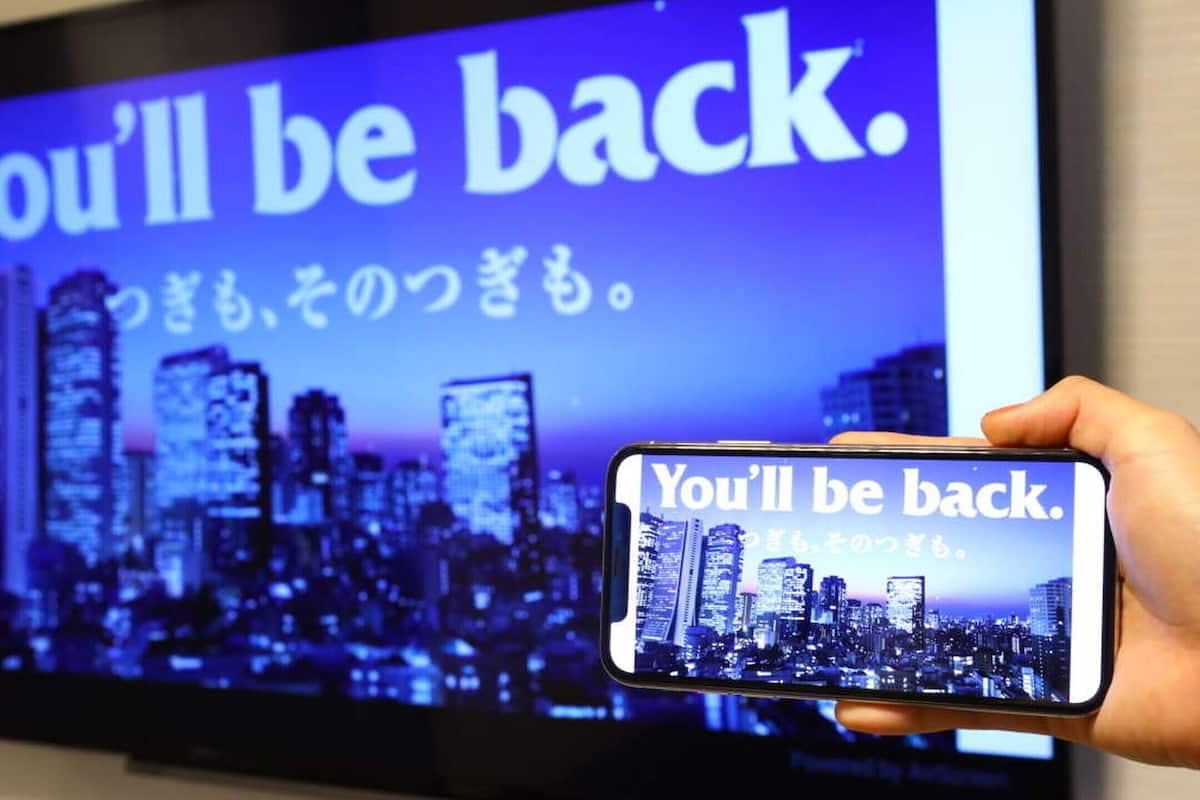 Un smartphone affichant le message « Vous reviendrez » sur un fond représentant un paysage urbain.