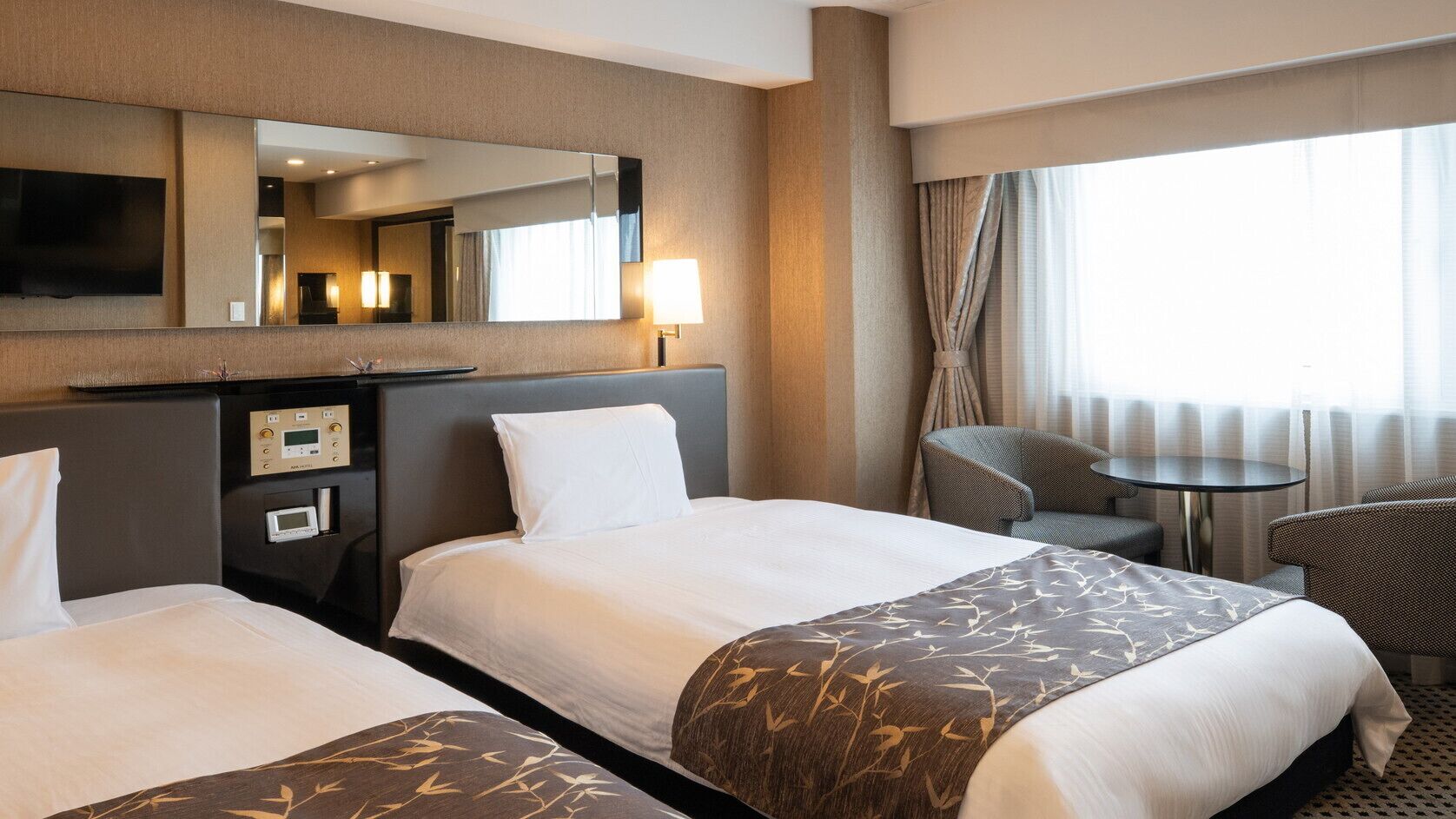 Habitación de hotel con dos camas, un escritorio, televisión de pantalla plana, una silla y una mesita.