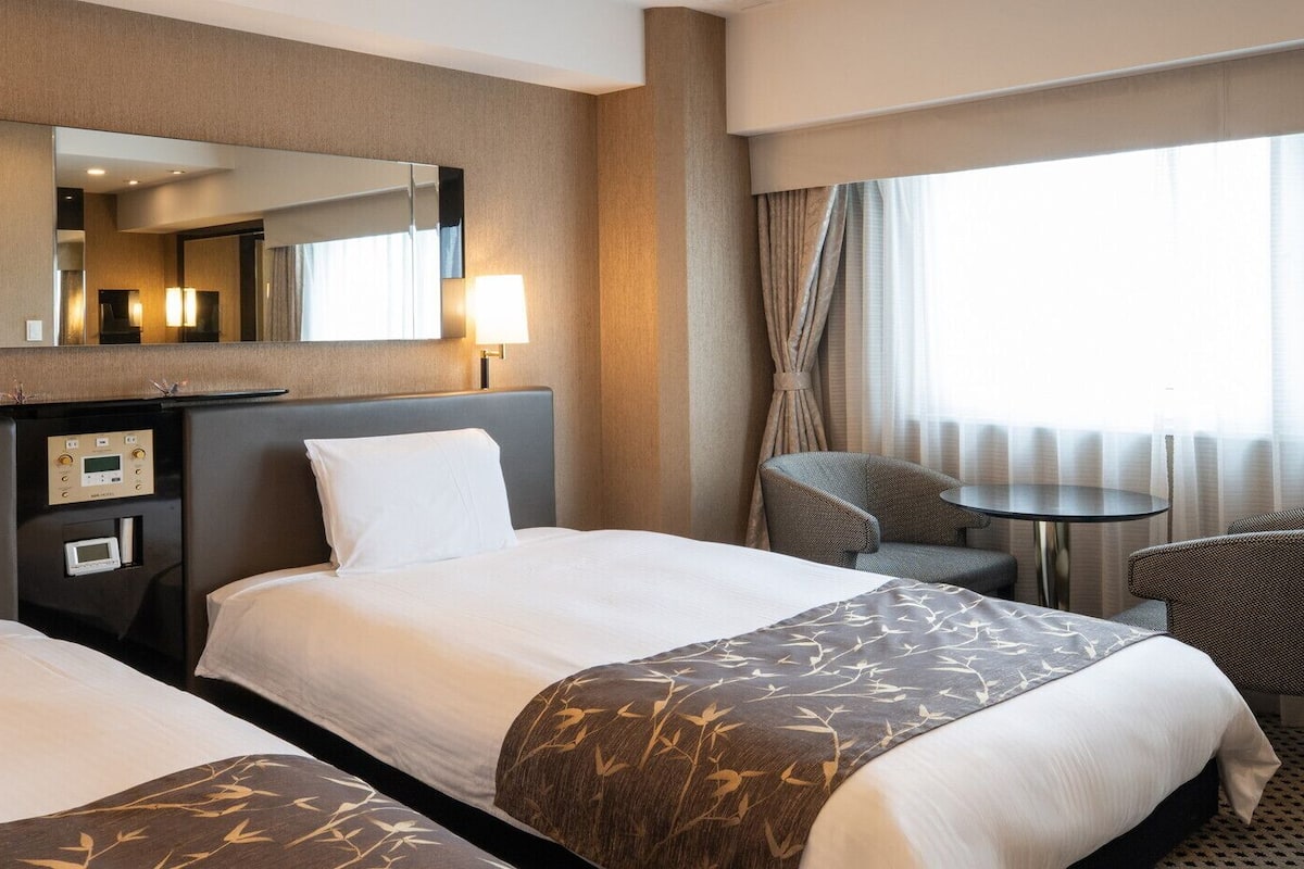 Une chambre d’hôtel avec deux lits, un bureau doté d’un téléviseur à écran plat, une chaise et une petite table.
