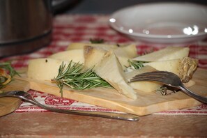 A wooden cutting board with sliced cheese and rosemary on a red and white checkered tablecloth. - B&B Eremo Gioioso (Pontremoli)