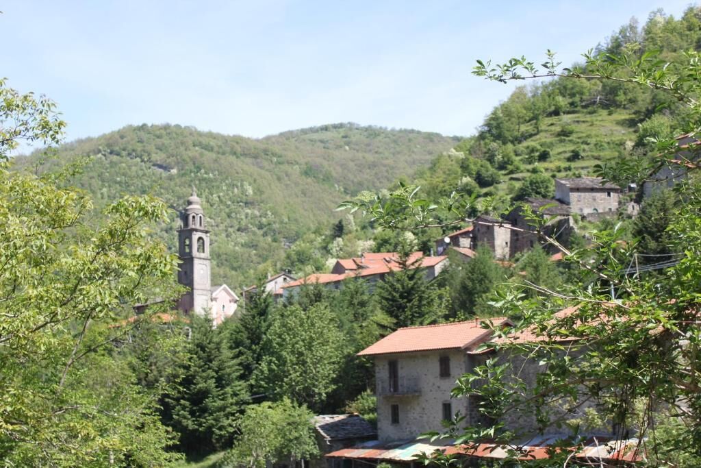 Un village aux bâtiments traditionnels en pierre, une église dotée d’un clocher et, en arrière-plan, de luxuriantes collines verdoyantes.